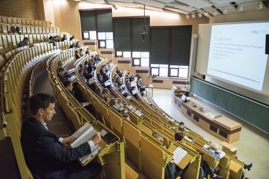 Ein halbgefüllter Hörsaal im Konrad-Zuse-Medienzentrum in Senftenberg. Vorne hält eine Referentin ein Mikrophon und steht vor einer Leinwand auf der eine Präsentation zu sehen ist. 