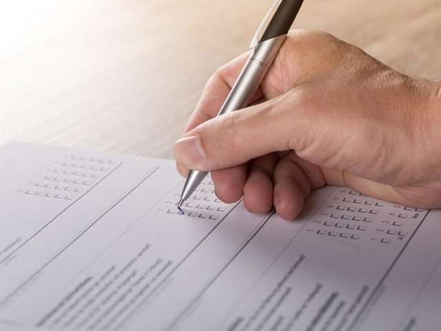 Hand hält Stift und ergänzt Text auf Blatt Papier