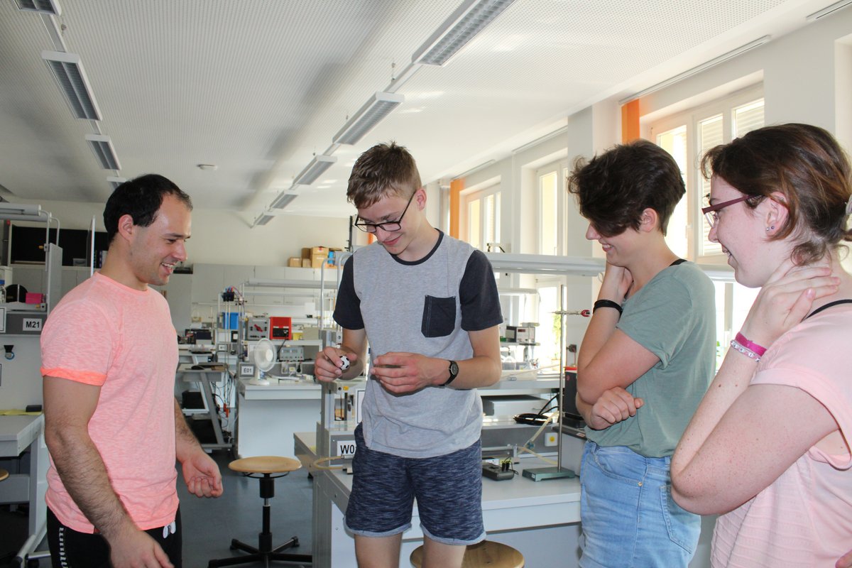 Drei Schüler und ein Laboringenieur im Physikalbor stehend, bei einem Experiment zur Aerodynamic mit kleinen Bällen.