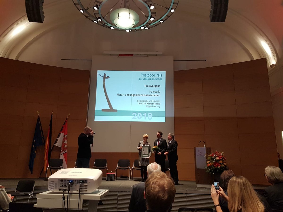 Die Ministerin präsentiert die Urkunde zur Auszeichnung der beiden diesjährigen Preisträger des Postdoc-Preises auf der Bühne