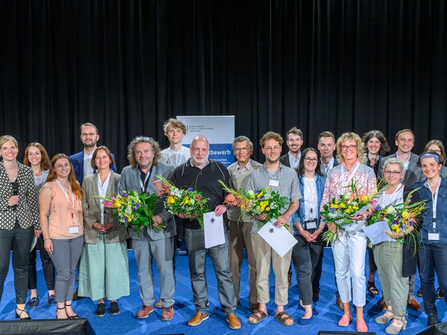 zweireihige Personengruppe, im Vordergrund die fünf Gewinner mit Blumensträußen