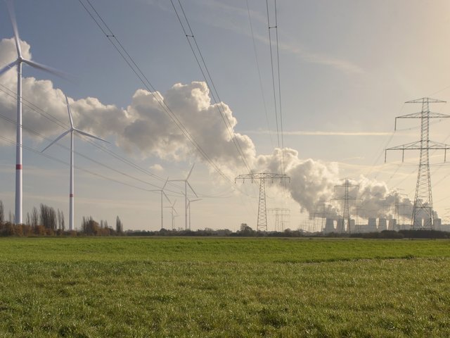Windräder auf einem Feld, im Hintergrund das Kohle-Kraftwerk Jänschwalde.