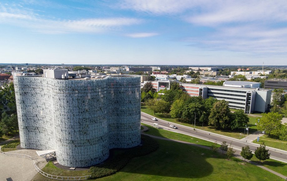 Luftaufnahme des Zentralcumpus der Brandenburgischen Technischen Univerität Cottbus-Senftenberg. Im Vordergrund steht das repräsentative Bibliotheksgebäude mit seiner amöben Form und der Glasfassade.. Im Hintergrund schließen sich das Hauptgebäude und weitere Gebäude an.