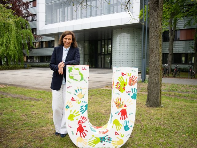 Präsidentin Prof. Gesine Grande mit dem großen "U" vor dem Hauptgebäude der Universität. Der Buchstabe wurde für die Präsentation von "VIELFALT LAUSITZ" am 18. Mai 2021 auf dem Cottbuser Altmarkt von BTU-Angehörigen gestaltet. (Foto: BTU, Spencer Vane)