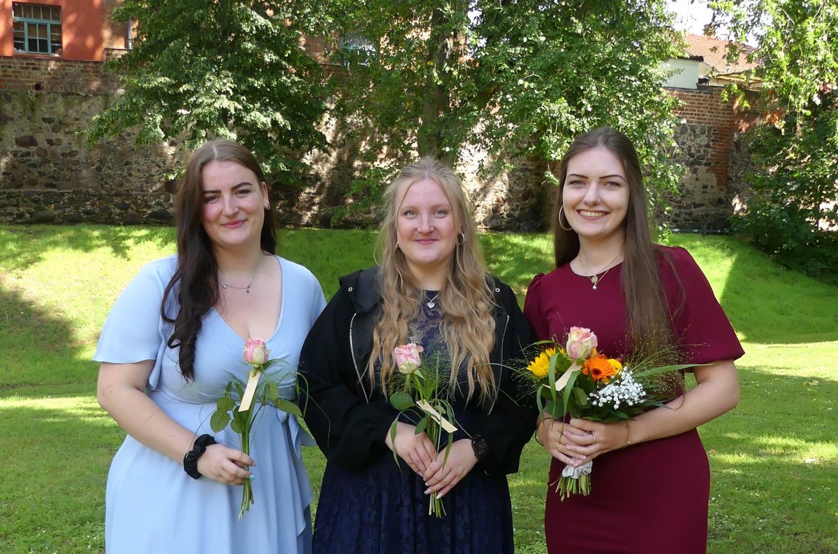 Die drei Absolventinnen mit Blumen und festlich gekleidet 