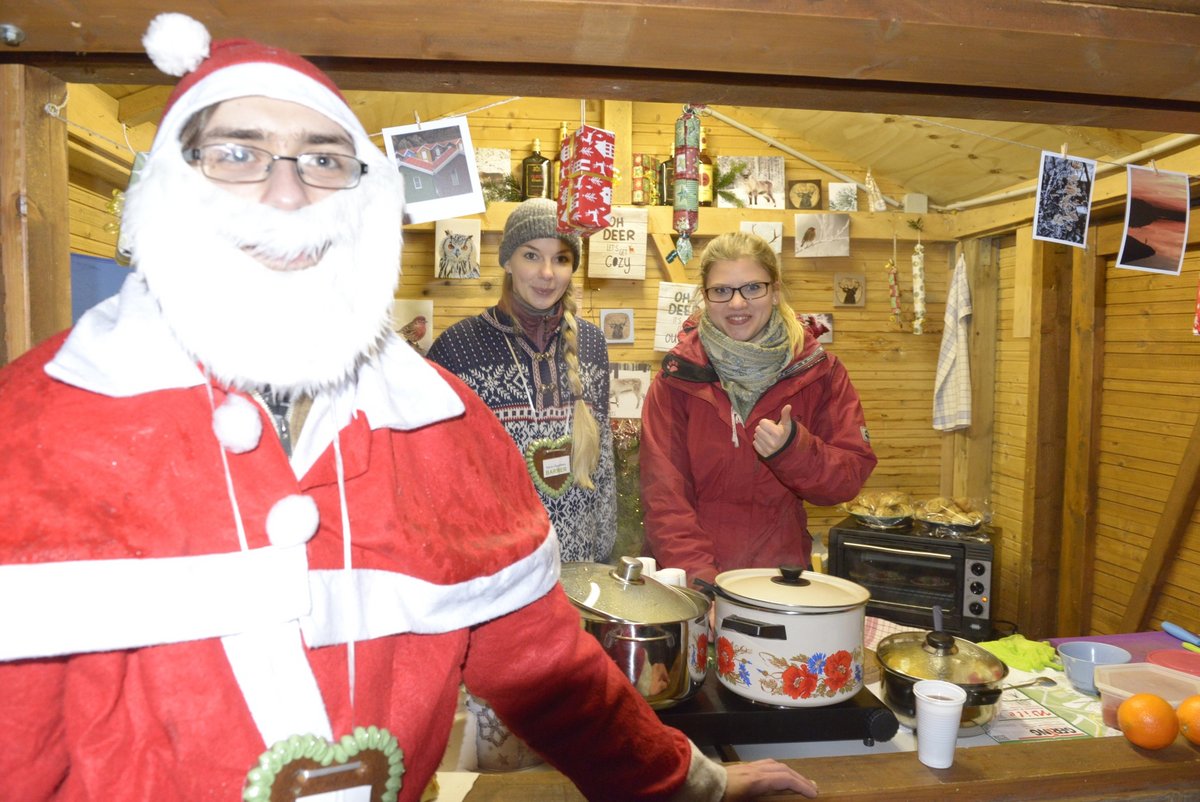 Studiernde präsentieren, in einer Weihnachtshütte stehend, ihre Angebote.