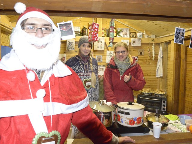 Studiernde präsentieren, in einer Weihnachtshütte stehend, ihre Angebote.