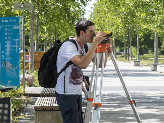Student mit einem Vermessungsgerät auf dem BTU-CampusBE