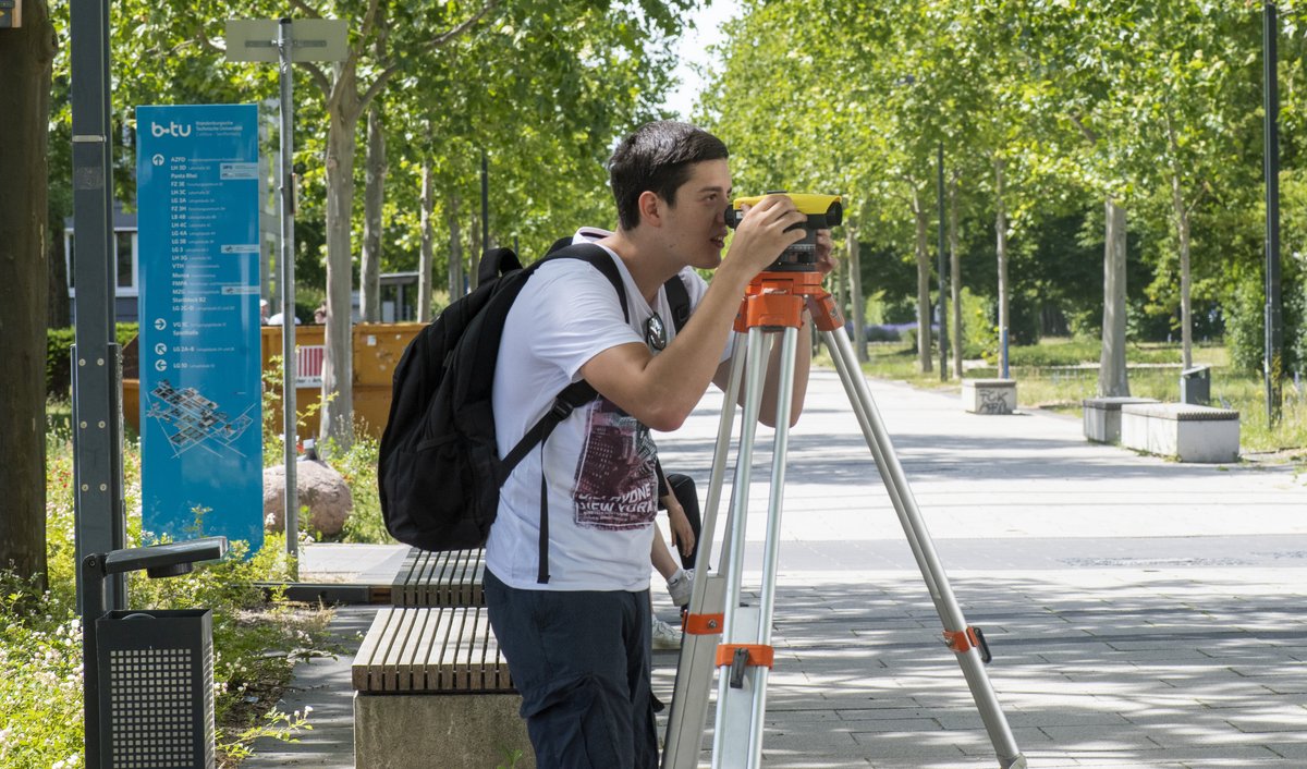 Student mit einem Vermessungsgerät auf dem BTU-CampusBE
