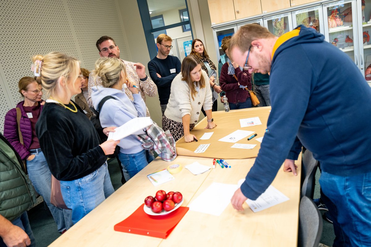 Das Foto zeigt Teilnehmende in einem Workshop. Auf dem Tisch liegen Arbeitsmaterialien.