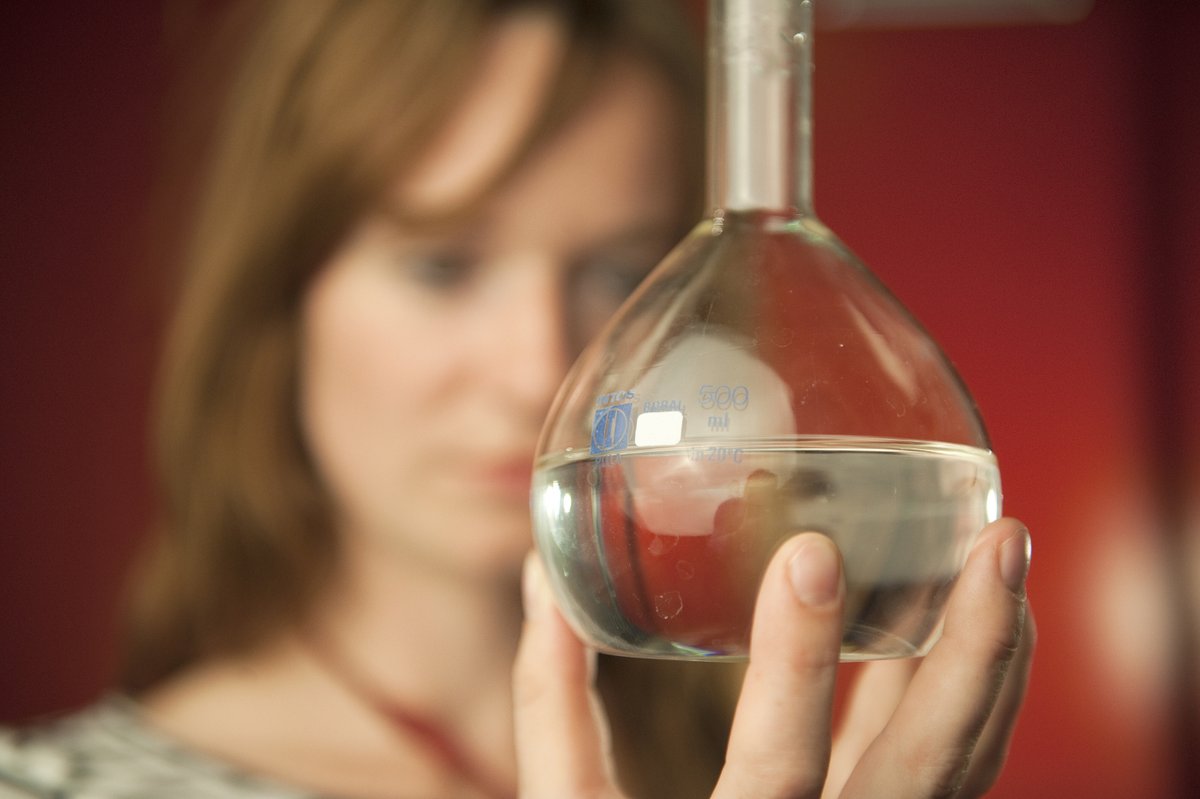 Das Gesicht einer Frau ist im Hintergrund, eine Hand hält einen Chemiekolben mit einer klaren Flüssigkeit, Synonym, Plakat mit Ausschreibungstext für den diesjährigen MINT-Preis der BTU