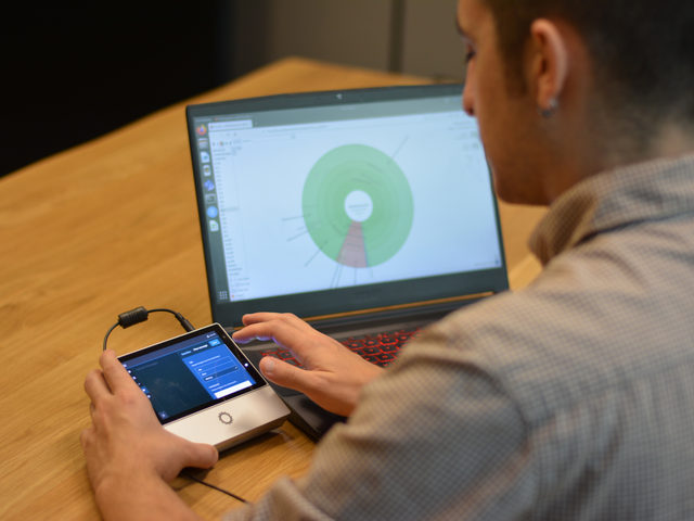 Adriel Latorre (Direktor der Genomikabteilung bei Darwin Bioprospecting) im Umgang mit einem DNA-Sequenzierer (Modell MinION). Im Hintergrund die Visualisierung eines Krona-Plots auf einem Laptop, die das taxonomische Profil einer der in der Studie entnommenen Schlammproben zeigt