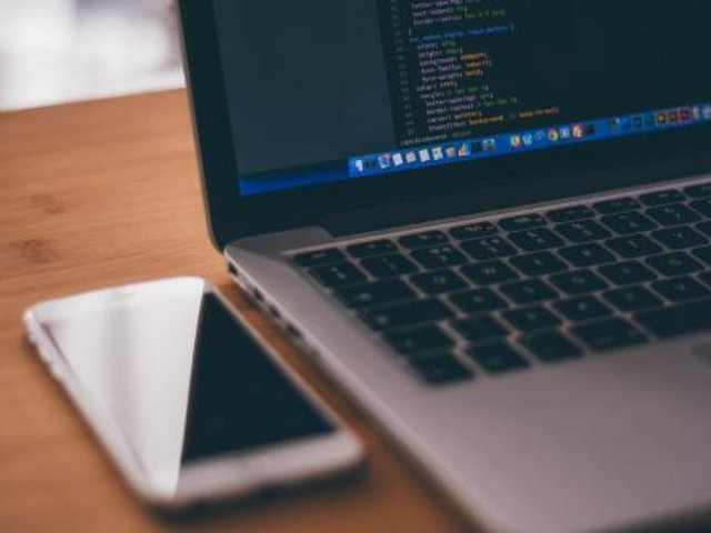 Aufgeklappter Laptop, daneben ein Handy auf einem Tisch