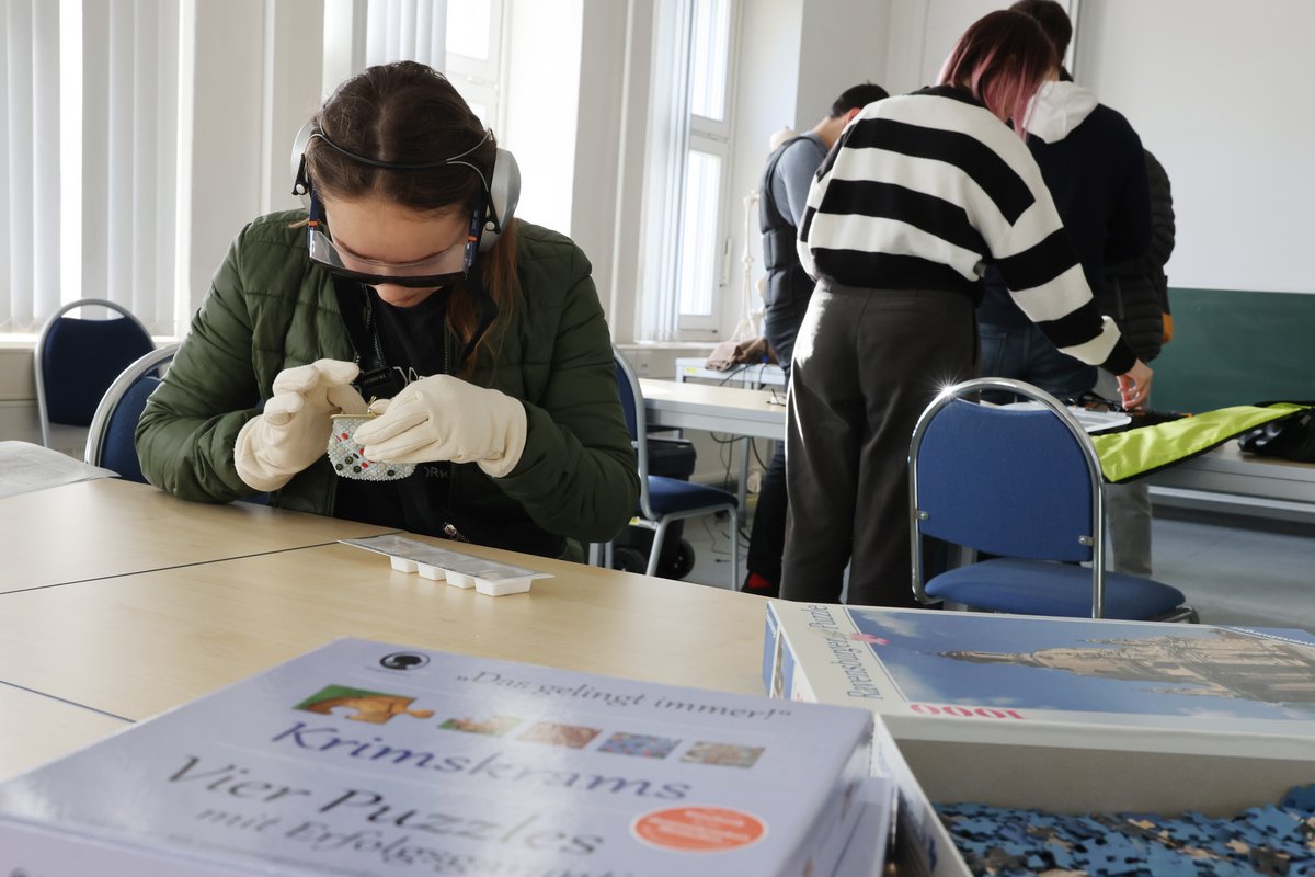 Eine Studieninteressierte empfindet in speziellen Handschuhen und im Umgang mit einem kleinen Gefäß die Feinmotorik im Alter nach. Foto: Steffen Rasche