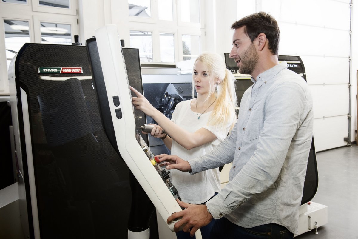 Eine Studentin und ein Student einer CNC-Fräse stehend, beim Programmieren.