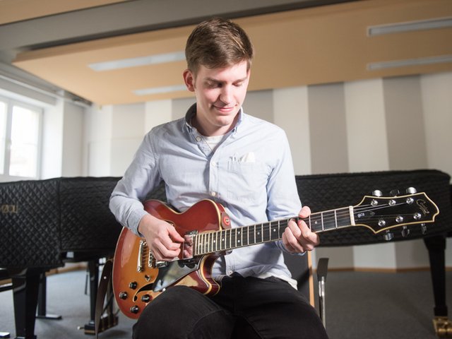 Student mit Gitarre im Konzertsaal