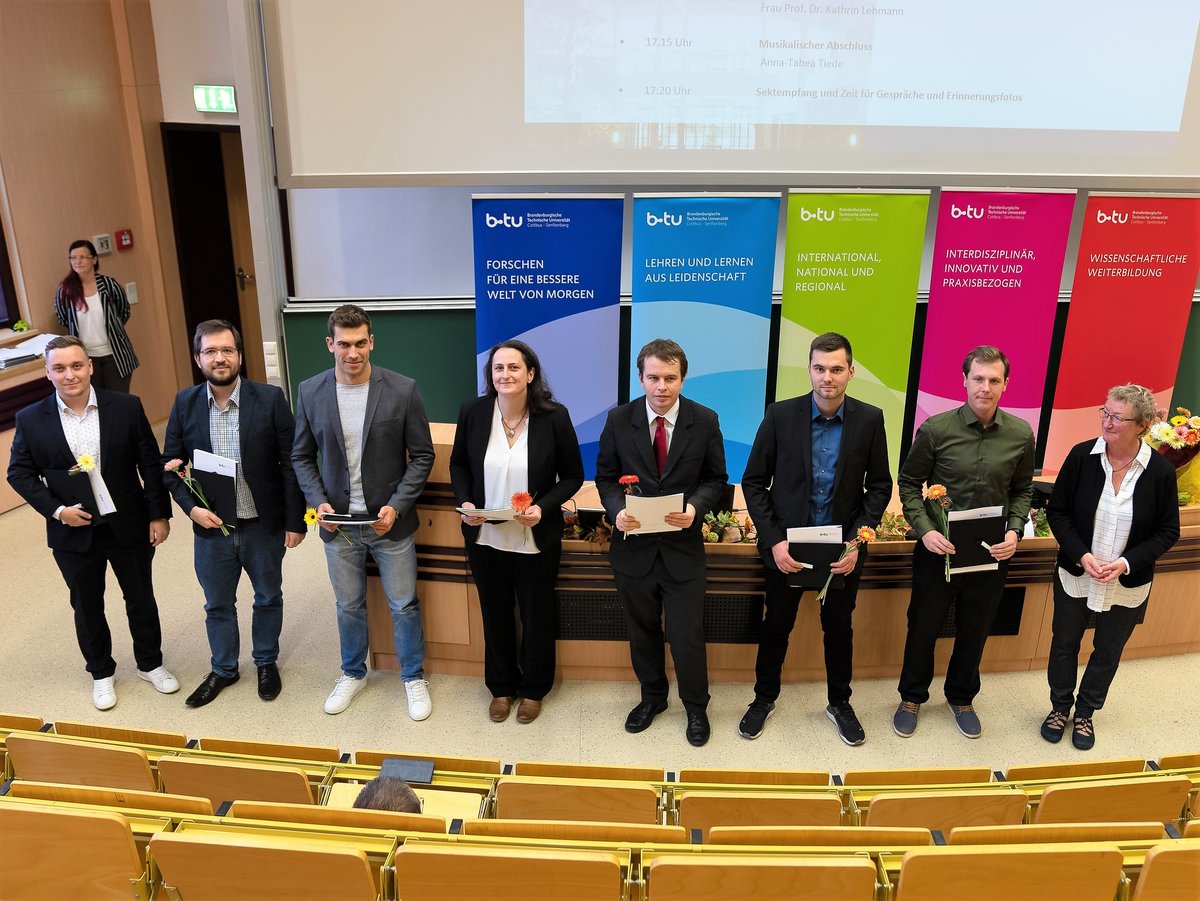 Graduates stand in the lecture hall with their certificates.