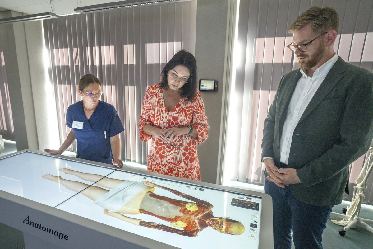 Gesunheitsministerin Britta Müller an einem digitalen Seziertisch, desse Funktionsweise Prof. Dr. Christian Kopkow und die akademische Mitarbeiterin Lisa Scholz vorführen.