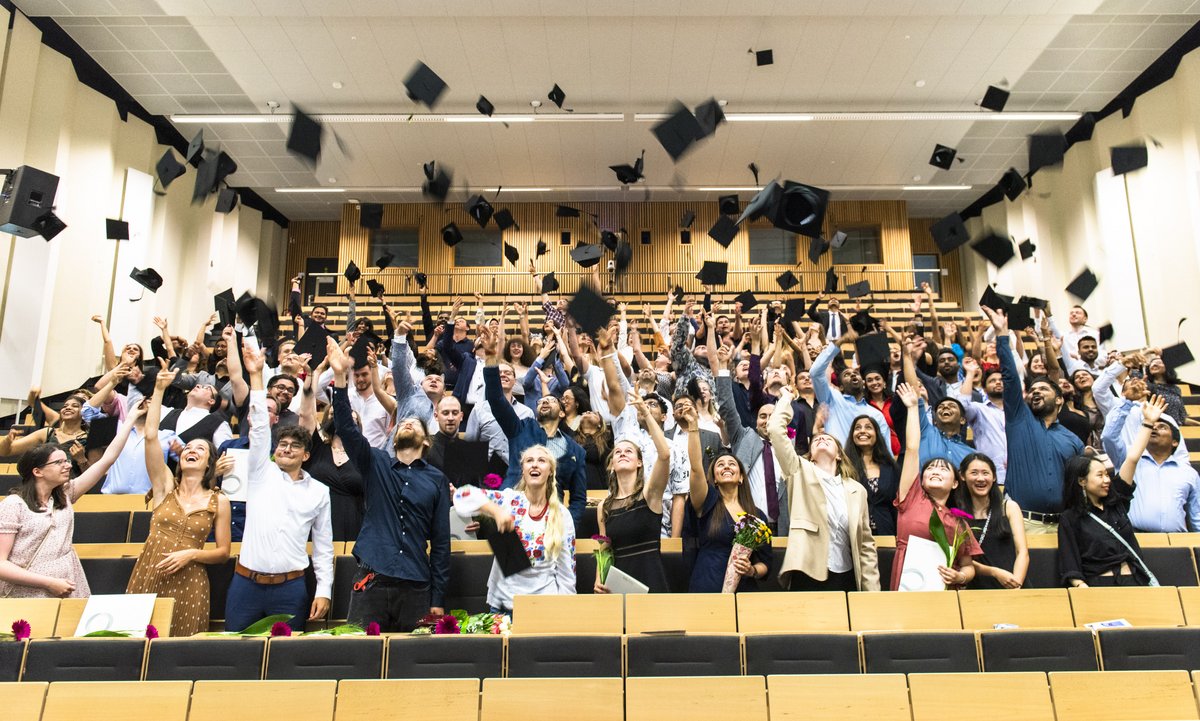 Studierende im Hörsaal werfen ihre Absolventenhüte in die Luft