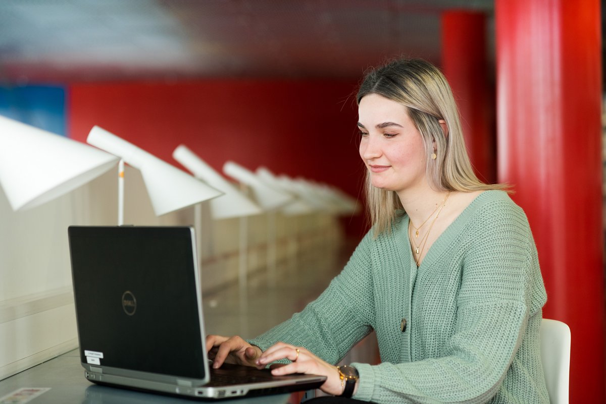Junge Frau sitzt schreibend vor einem Laptop.