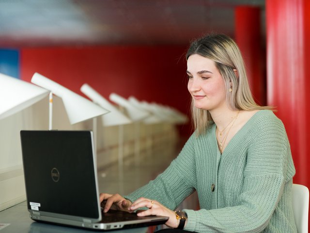 Junge Frau sitzt schreibend vor einem Laptop.