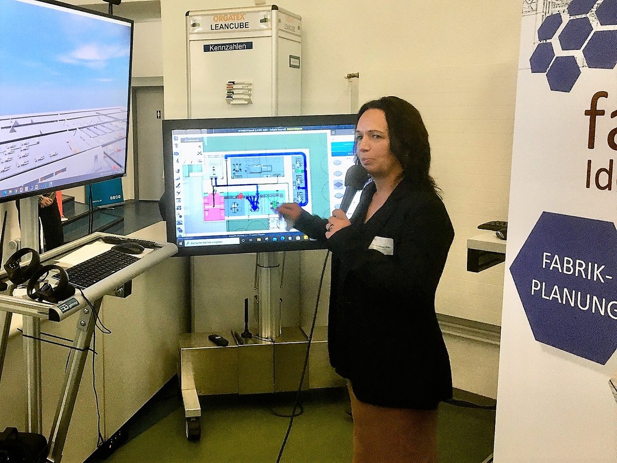 Prof. Dr.-Ing. Peggy Näser, standing in front of two monitors, gives explanations in the Efficient Factory Center. Photo: BTU, Ralf-Peter Witzmann