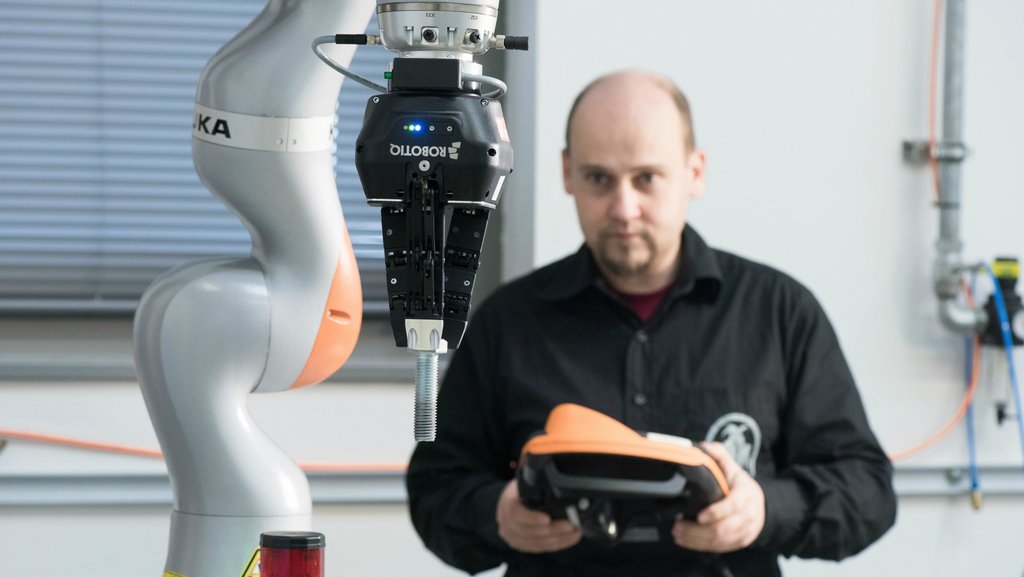 Ein Kollege aus dem Fachgebiet Automatisierungstechnik steuert ein Roboterarm.