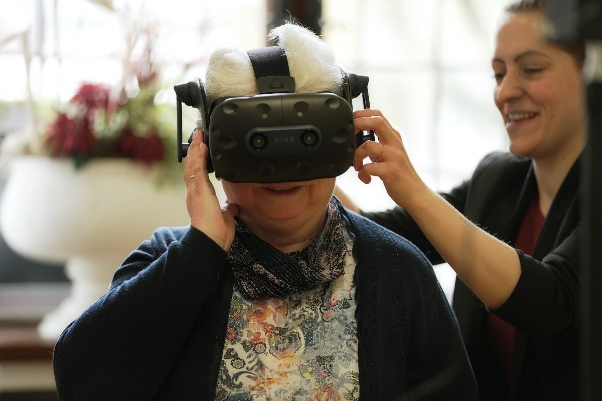 Wissenschaftlerin passt älterer Dame eine VR-Brille an