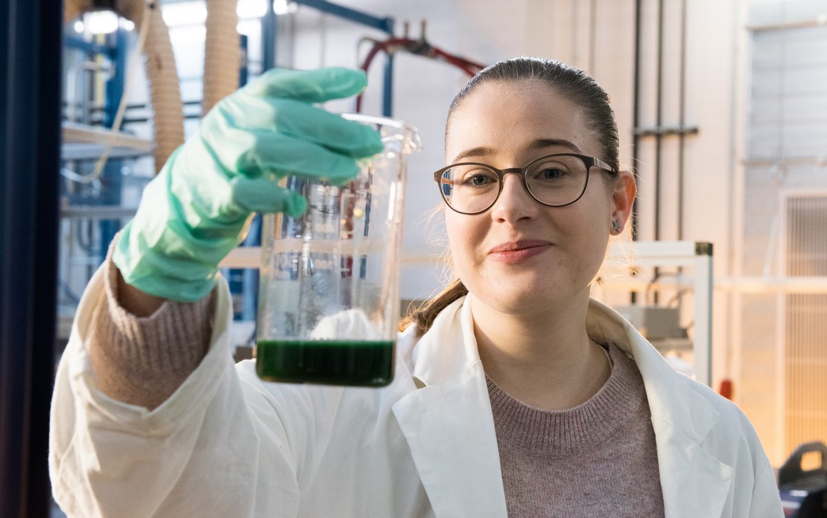 Portraitfoto der Studentin, die einen Glasbehälter mit einer Algensuspension in der Hand hält