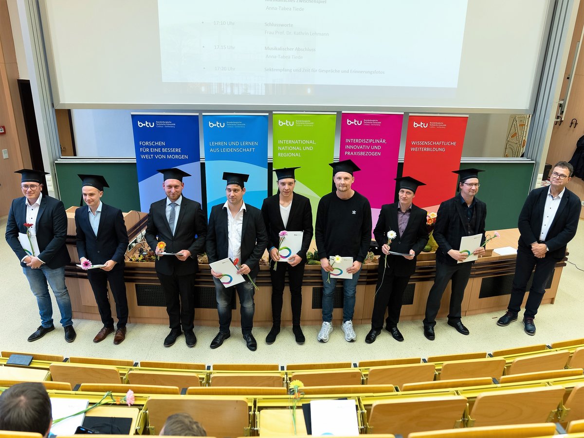 Graduates stand in the lecture hall with their certificates.