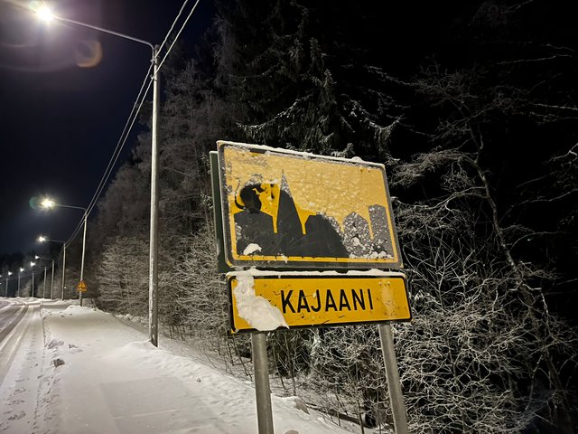 Das Foto zeigt das Ortseingangeschild von Kajaani (Finnland), schwarze Silhouette der Stadt auf gelben Untergrund.