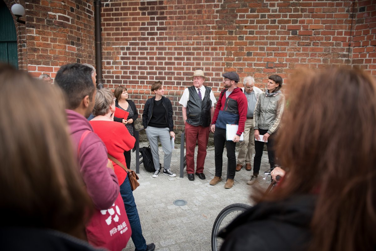 Auf dem Bild ist eine Gruppe Menschen vor der roten Ziegelwand der Oberkirche in Cottbus zu sehen.