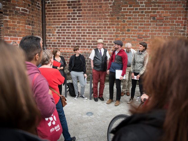 Auf dem Bild ist eine Gruppe Menschen vor der roten Ziegelwand der Oberkirche in Cottbus zu sehen.