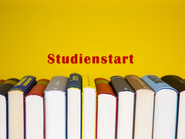 Das Foto zeigt vor einem gelben Hintergund aufgstellte Bücher und den Schriftzug Studienstart.