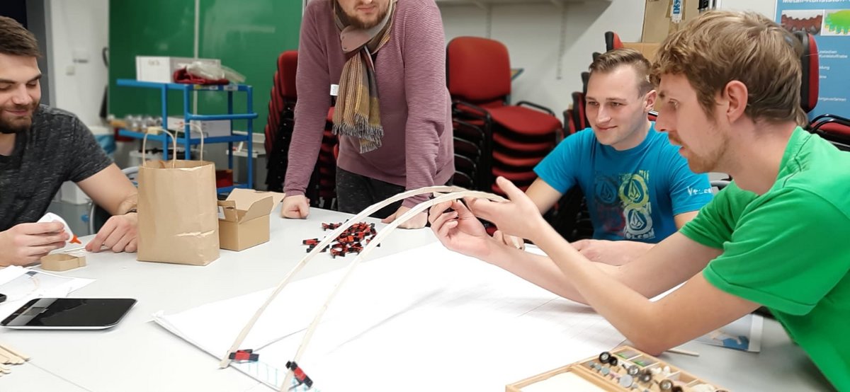 Studierende beim Bau einer Brücke aus Eisstielen und Leim