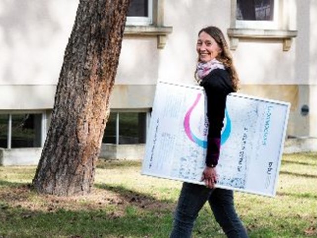 Professorin Doktorin Juliane Noack Napoles mit einem Plakat der Veranstaltung Eudaimogenese - Gelingendes Leben ermöglichen