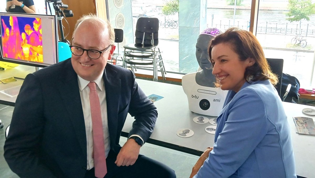 Die Bundesministerin für Forschung, Technologie und Raumfahrt Dorothee Bär und der Parlamentarische Staatssekretär Matthias Hauer sitzen am Stand der BTU vor dem humanoiden Roboter Ami.
