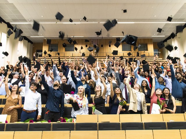 Studierende im Hörsaal werfen ihre Absolventenhüte in die Luft