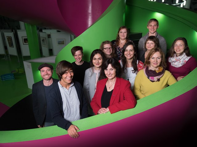 Das Team der Forschungsplattform ist mit insgesamt 12 Mitarbeitern auf der Treppe der Unibibliothek abgebildet