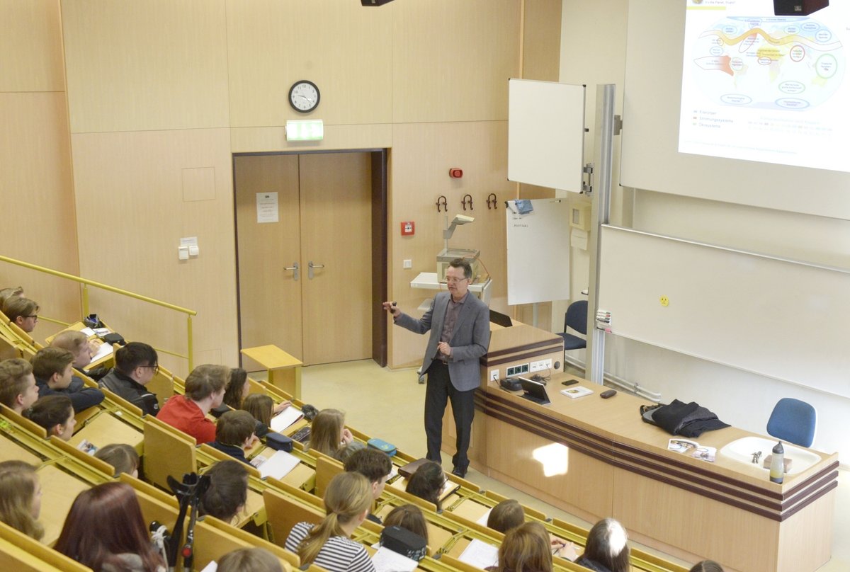 Schülerinnen und Schüler folgen, im Hörsaal sitzend, dem Eröffnungsvortrag von Prof. Dr. Jan-Heiner Küpper.