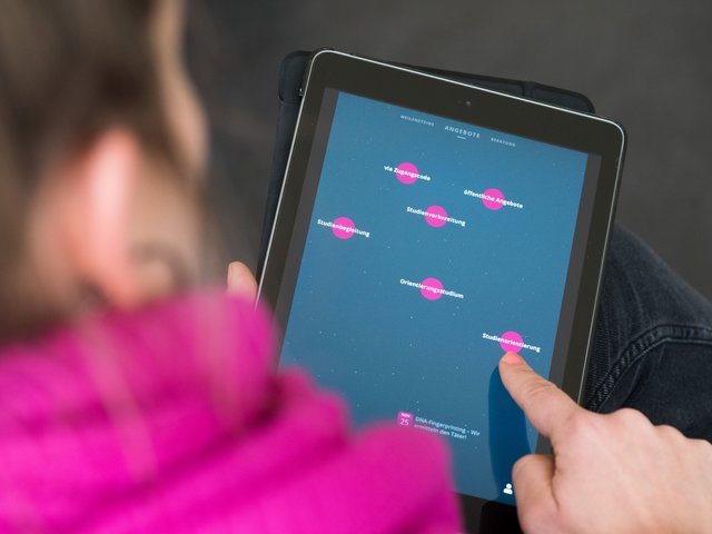 Eine weibliche Person betrachtet die auf einem Tablet abgebildete Benutzeroberfäche der Online-Plattform „EDUpilot“.