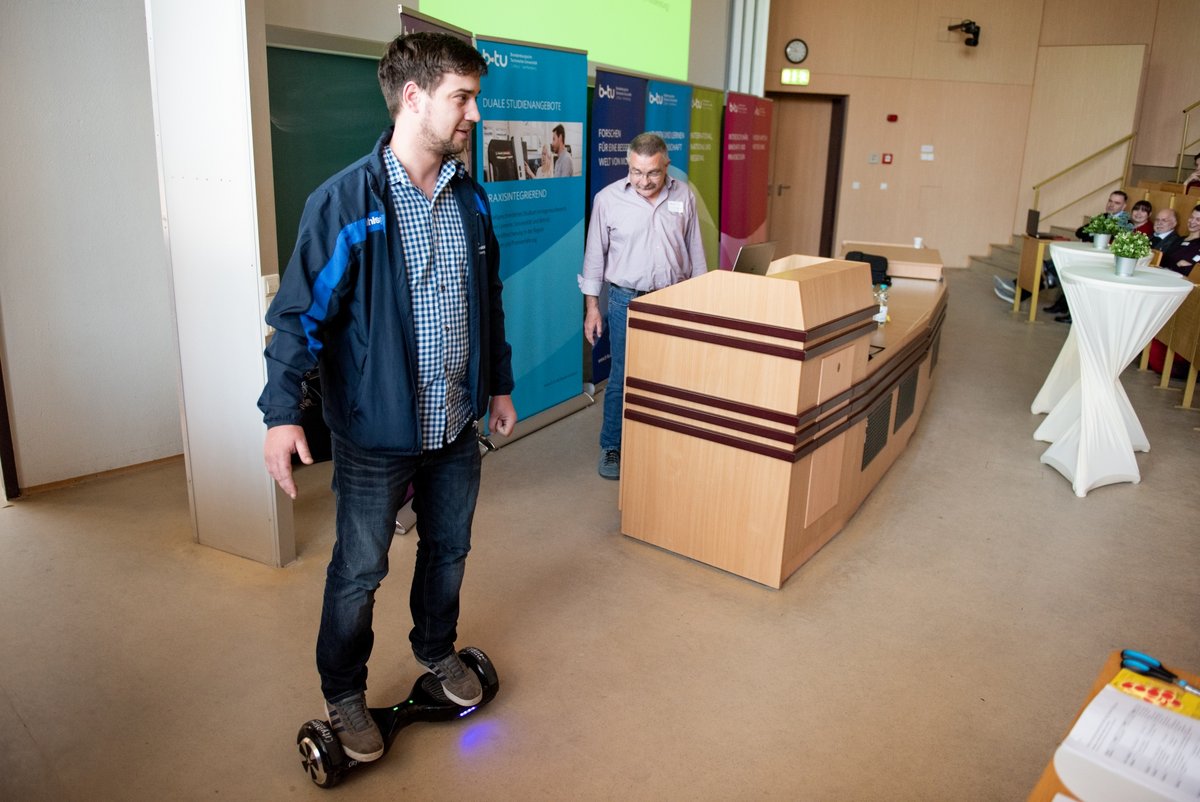 Vorstellung der Studienangebote anhand origineller Praxisbeispiele. Maschinenbau-Master-Student Daniel Britz steht auf einem E-Board, und der Studiengangsleiter der Elektrotechnik, Prof. Dr. Erhard Stein, gibt Erläuterungen.