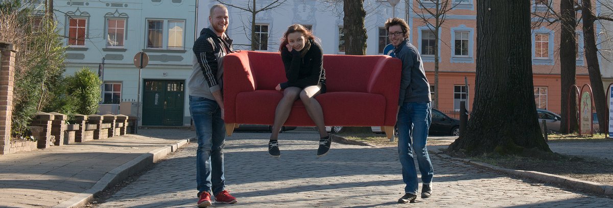 two students carrying another student through the Cottbus Old Town on a sofa