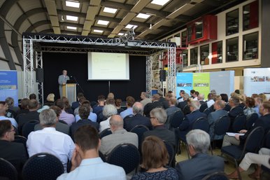 Prof. Dr.-Ing. Jörg Steinbach, Präsident der BTU Cottbus-Senftenberg, eröffnet den 1. BTUTransferTag mit einer Rede in der Panta Rhei Halle. Er steht auf einer Bühne hinter einem Rednerpult. Vor ihm die Teilnehmerinnen und Teilnehmer auf Stühlen sitzend und dem Fotografen mit den Rücken zugewandt.