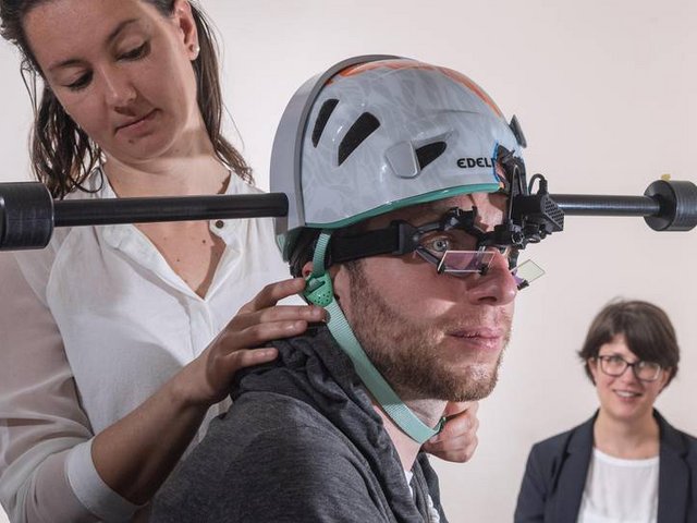 Dr. Cecilia Ramaioli (links) überprüft den Sitz des Helms mit Gewichten bei einem Probanden. Prof. Nadine Lehnen stellt im Hintergrund den Computer für das Experiment ein