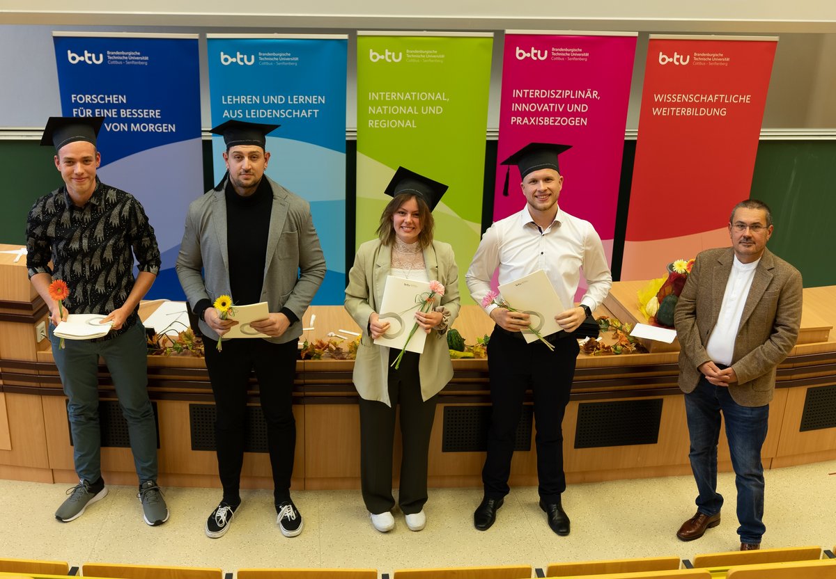 Graduates stand in the lecture hall with their certificates.