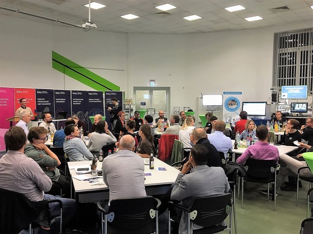 Jungunternehmerinnen und -unternehmer vom Netzwerk NEOpreneurs sitzen im Zentrum Effiziente Fabrik an der BTU in Senftenberg an Tischen und fplgen einem Vortrag.