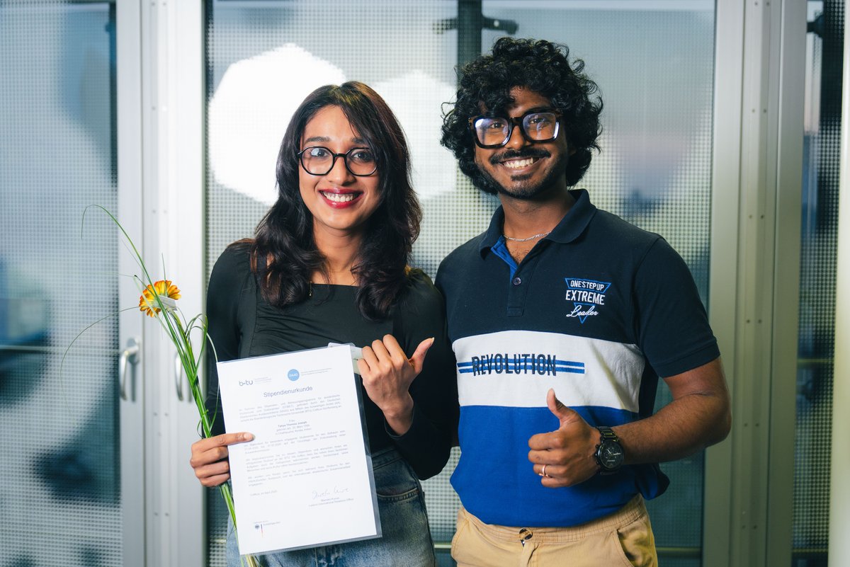 Eine Stipendiatin und ein Stipendiat lachend mit Urkunde in der Hand