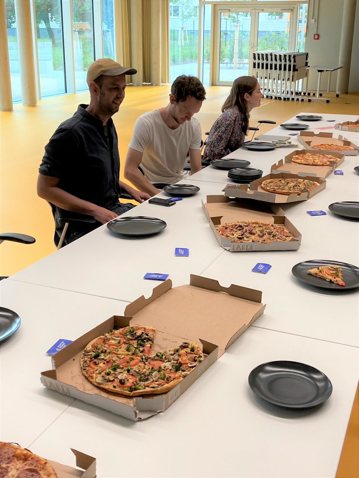 Menschen sitzen am Tisch, sprechen und essen Pizza
