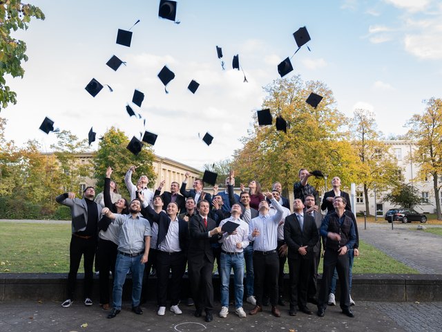 Ehemalige Studierende werfen ihre Absolvent*innenhüte in die Luft.